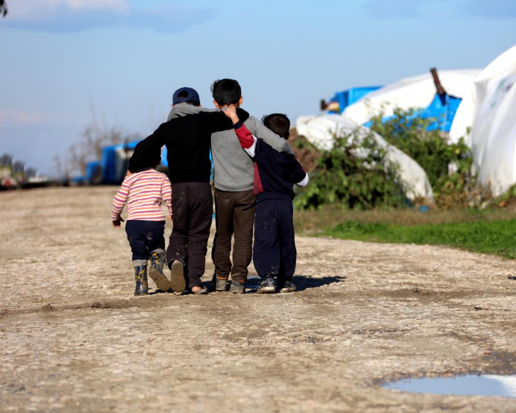 Vier kinderen lopen elkaar omhelzend, weg van de camera, over een zandweg