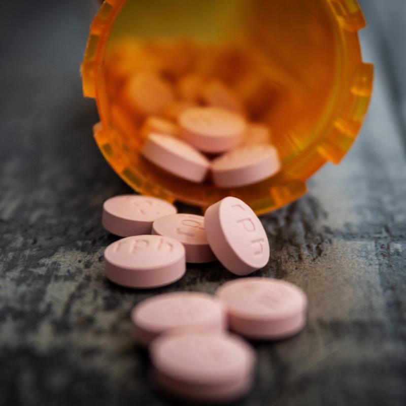 Een oranje pillendoosje met roze pillen erin ligt op de grond. 